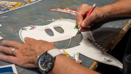 A person uses a craft knife to cut out a large, white, cartoon-style molar shaped tooth on a work table.